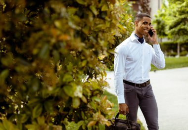 Yakışıklı Afro-Amerikan iş adamı sokakta yürürken cep telefonu kullanıyor.