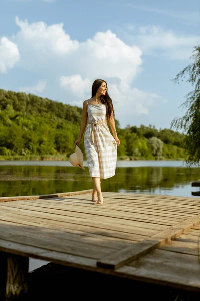暑い夏の日に穏やかな湖で木製の桟橋を歩く若い女性 — ストック写真