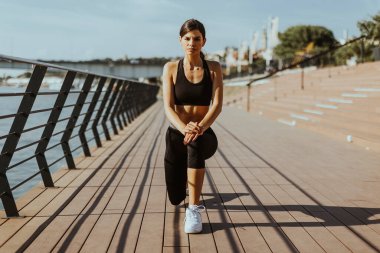 Spor giyimli güzel bir kadın nehir kenarında egzersiz yapıyor.
