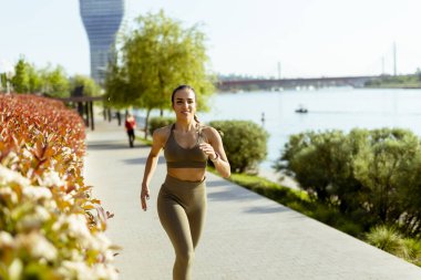Güzel genç bayan nehir kenarında koşuya çıkıyor.