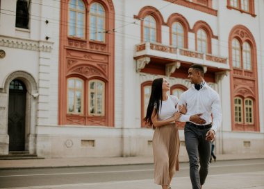 Sokakta yürüyen yakışıklı, etnik çeşitlilikte genç bir çift.