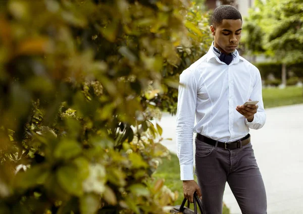 Handsome young African American businessman using a mobile phone while walking on a street