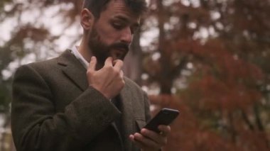 Güz parkında cep telefonu kullanan yakışıklı genç adam.