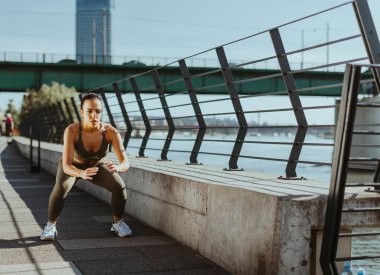 Spor giyimli güzel bir kadın nehir kenarında egzersiz yapıyor.