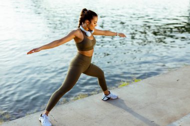 Spor giyimli güzel bir kadın nehir kenarında esniyor.