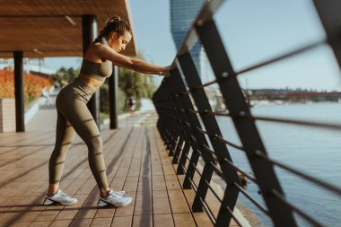 Spor giyimli güzel bir kadın nehir kenarında egzersiz yapıyor.