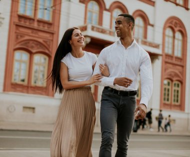 Sokakta yürüyen yakışıklı, etnik çeşitlilikte genç bir çift.