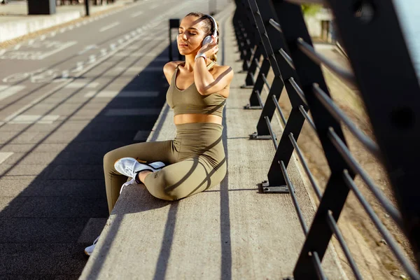 在城市地区跑步后 戴耳机的年轻貌美的女人休息一下 — 图库照片