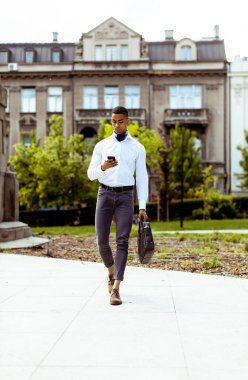 Yakışıklı Afro-Amerikan iş adamı sokakta yürürken cep telefonu kullanıyor.