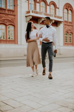 Sokakta yürüyen yakışıklı, etnik çeşitlilikte genç bir çift.