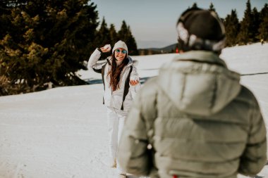 Genç bir çift dağda güneşli bir günde kartopu savaşı yapıyor.