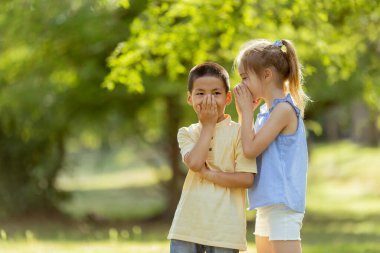 Caucasian girl telling secret to asian boy in the park on a sunny day