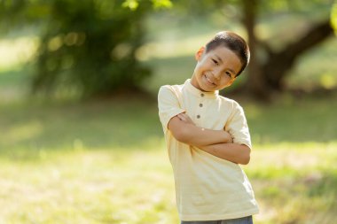 Güneşli bir günde parkta dikilen sevimli Koreli çocuk.