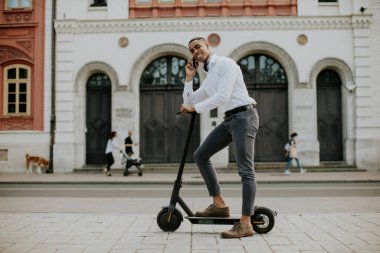 Sokakta elektrikli scooterla dururken cep telefonu kullanan yakışıklı Afrikalı genç bir Amerikalı.