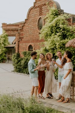 Bir grup mutlu genç dışarıda içkiyle eğleniyor ve tezahürat yapıyor.