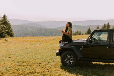 Pretty young woman relaxing on a terrain vehicle hood at countryside