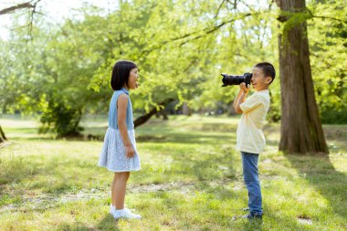 Cute little asian boy acting like a professional photographer while taking photos of his little sister