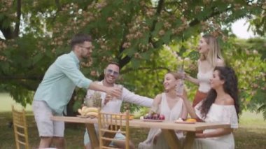 Taze limonatayla tezahürat yapan ve bahçede meyve yiyen bir grup mutlu genç.