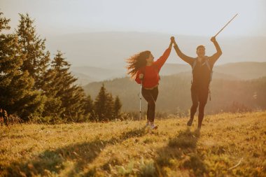 Sırt çantaları yeşil tepelerde yürüyen gülümseyen genç çift.
