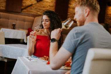 Yakışıklı genç çift restoranda beyaz şarapla yemek yiyor.