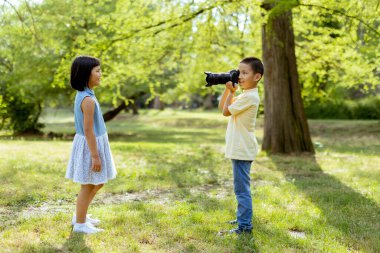 Cute little asian boy acting like a professional photographer while taking photos of his little sister