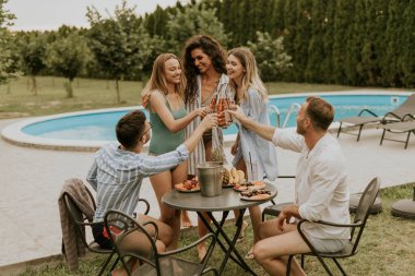 Group of happy young people cheering with cider by the pool in the garden