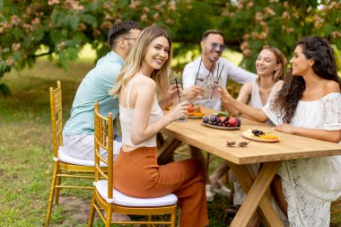 Group of young people cheering with fresh lemonade and eating fruits in the garden