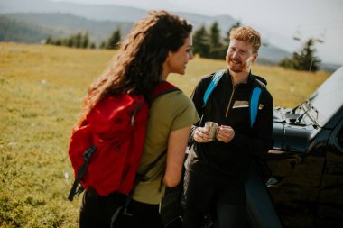 Handsome young couple relaxing by a terrain vehicle hood at countryside