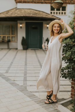 Pretty young woman with hat drinking cold lemonade in the resort garden