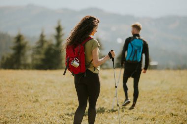 Sırt çantaları yeşil tepelerde yürüyen gülümseyen genç çift.