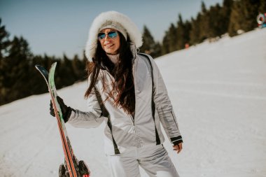 Güneşli bir günde kayak pistinde duran genç bir kadın.