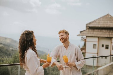 Handsome young  relaxing on the outdoor terrace and drinking fresh orange juice
