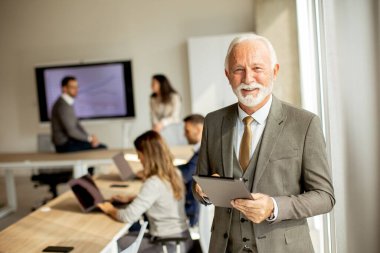 Ofiste dijital tablet üzerinde çalışan yakışıklı kıdemli iş adamı.