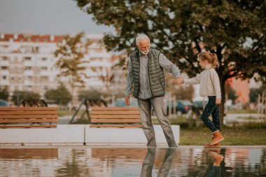 Yakışıklı büyükbaba sonbahar günü parkta küçük su havuzunda torunuyla vakit geçiriyor.