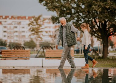 Yakışıklı büyükbaba sonbahar günü parkta küçük su havuzunda torunuyla vakit geçiriyor.