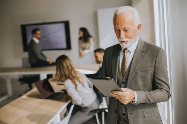Ofiste dijital tablet üzerinde çalışan yakışıklı kıdemli iş adamı.