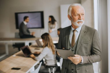 Ofiste dijital tablet üzerinde çalışan yakışıklı kıdemli iş adamı.