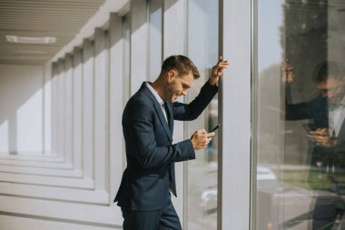 Modern ofis koridorunda cep telefonu kullanan yakışıklı bir iş adamı.