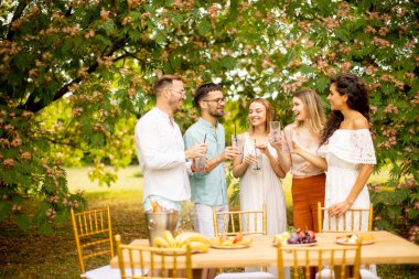 Group of young people cheering with fresh lemonade and eating fruits in the garden