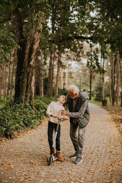 Senior Uczy Wnuczkę Jeździć Hulajnodze Jesiennym Parku — Zdjęcie stockowe
