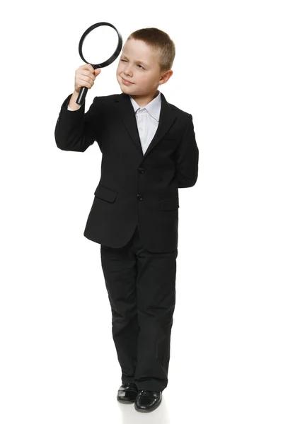 Full length of a schoolboy in black suit looking through the magnifying glass — Stock Photo, Image