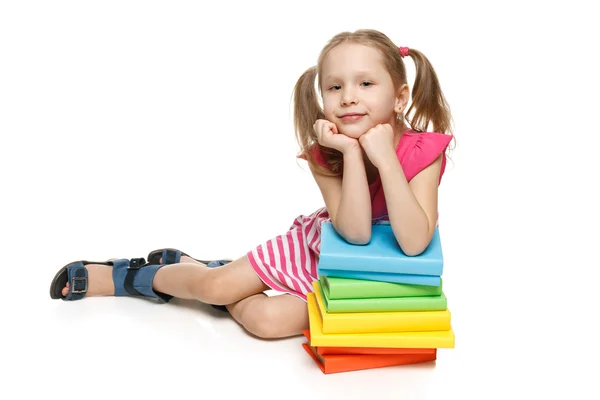 Niña sentada en el suelo apoyada en la pila de libros — Foto de Stock