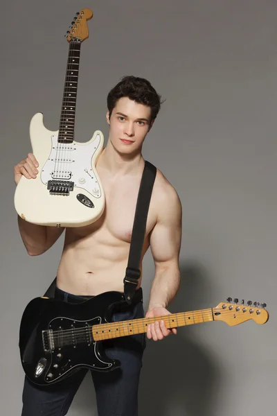 2 つのエレク トリック ギターを渡す裸の胴体を持つ若い筋肉の男 — ストック写真
