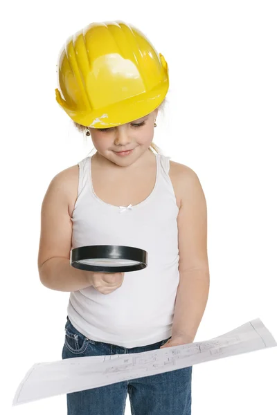 Девушка строитель в желтом шлеме анализирует рисунок через увеличительное стекло — стоковое фото