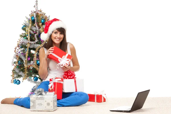 Girl sitting near Christmas tree with many gifts and laptop — Stock Photo, Image