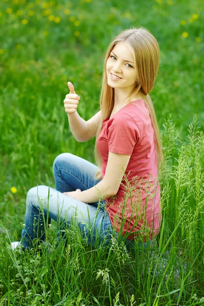 Mujer sonriente sentada al aire libre haciendo gestos con el pulgar hacia arriba —  Fotos de Stock