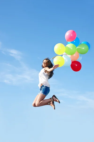 Happy young woman jumping with colorful balloons — Stock Photo, Image