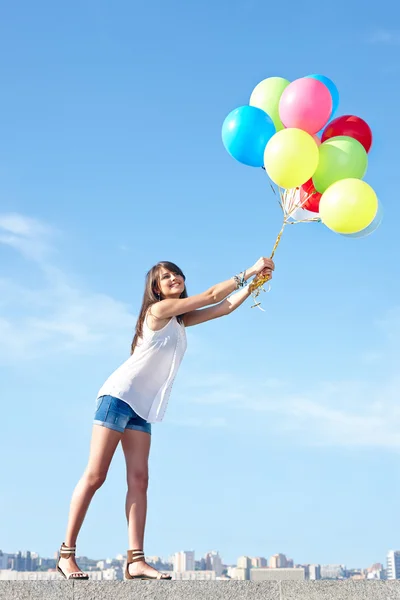 Happy young woman flying away with balloons — Stock Photo, Image