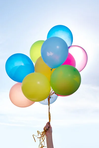 Mano sosteniendo racimo de globos de colores en el cielo azul —  Fotos de Stock