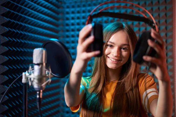 Meisje in opnamestudio in hoofdtelefoon met microfoon over absorberende paneel achtergrond met gesloten ogen — Stockfoto